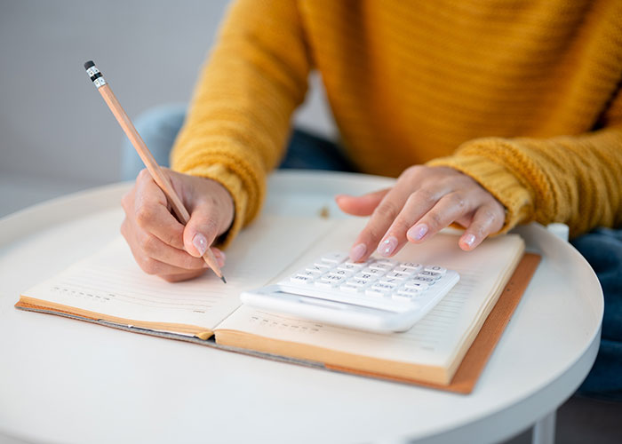 Person using a calculator and writing notes to track income and living expenses