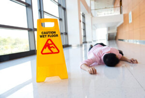 Person lying on the floor next to a wet floor sign